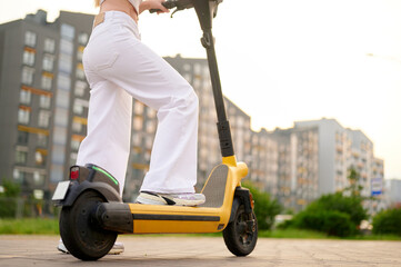 urban commuting energy woman riding yellow electric scooter through city streets. white pants and...