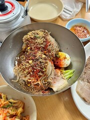 Naengmyeon, a refreshing Korean cold noodle dish served in an icy broth, topped with sliced vegetables, a boiled egg, and spicy sauce. Perfect for summer food photography and Korean cuisine projects.