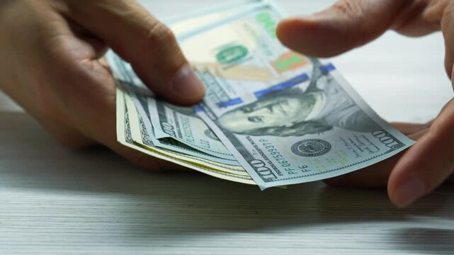 Counting money at a cash register in a bank.
American dollars in the hands of a bank client and payment of taxes.
Man recounts money savings and finances.
Financial worker with American dollars