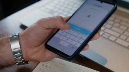 Close-up of a businessman hand wearing a watch, using a mobile banking app to send money, with a laptop in the background. - Powered by Adobe