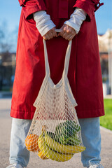 Woman is holding a reusable mesh bag filled with fresh produce. Embracing a sustainable and...