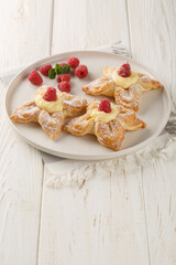 Puff flower-shaped cake with custard cream and fresh raspberries close-up in a plate on the table. Vertical