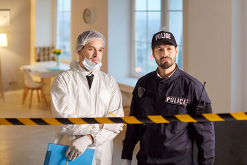 Portrait of a policeman and criminologist standing together at a crime scene during an...