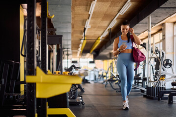 Happy sportswoman using mobile phone while walking through gym.