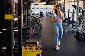 Happy athletic woman using app on smart phone during gym workout.