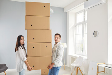 Surprised and happy couple moving a large stack of boxes together during relocation to a new home...