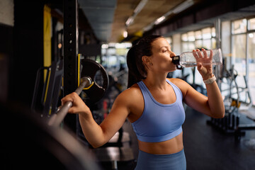 Thirsty athlete drinking water during her strength training in gym.