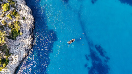 Plan de vue aérien sur un bateau en plein milieu de la mer Méditerranée vers des falaises avec une eau bleue et turquoise  