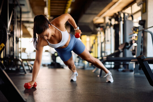 Athletic woman doing plank exercise with hand weights in gym.