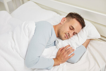 Man sleeping in his bed. Young man seeing dreams while still asleep in the morning. Adult man lying on his side on a soft white pillow and natural linen sheets in a comfortable bed in the bedroom