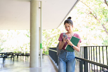 Online learning, e-education concept. Happy young asian lady student using phone outdoors, carrying backpack and textbooks, going to university, checking her schedule online.