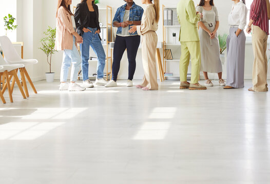 People communicate and share business ideas as they meet at networking event. Team of young diverse women in smart casual clothes standing in office and talking. Cropped shot, low section