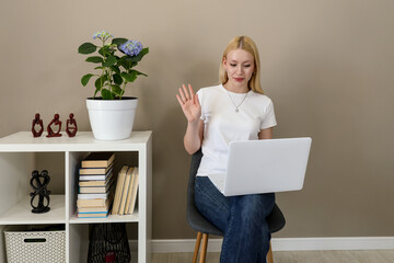 Woman waving at laptop screen during video call in home office