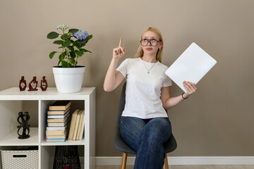 Woman with glasses holding laptop and pointing up with idea