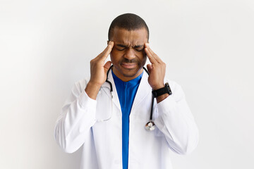 Stressed black doctor with hands on temples, eyes closed in pain. Young African American medical...