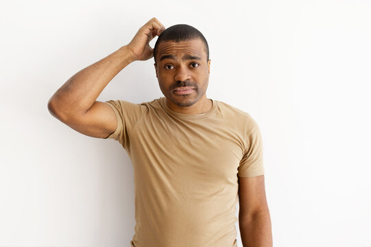 Confused black man scratching his head with uncertain expression. Representing doubt, question, or hesitation in casual neutral background setting, copy space