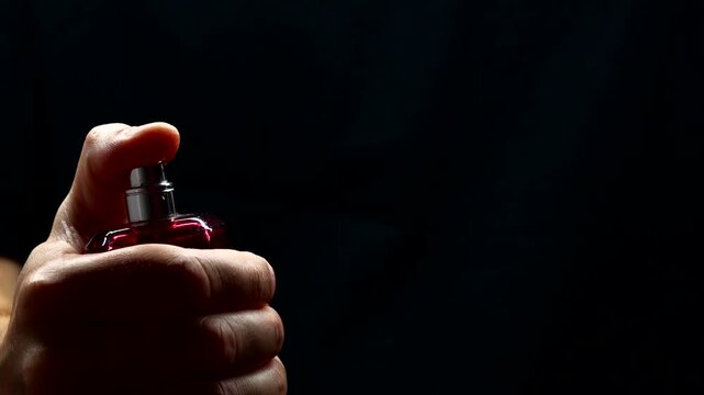 Spraying perfume on a black background.
A man sprays cologne, the drops scatter on a black background in slow motion.
Many small drops with backlight