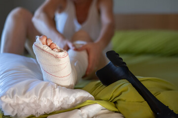 Close-up of a broken leg in a plaster cast resting on a pillow, with crutches nearby, as the...