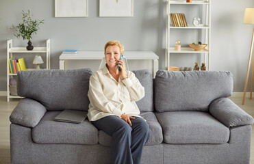 Cheerful elderly woman enjoying weekend leisure time at home, having a conversation on smartphone....