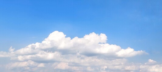 Wide view of blue sky with fluffy white clouds on a sunny day with peaceful spring ambiance background. Soft white clouds float in the clear blue sky. Clear blue sky, bright spring.
