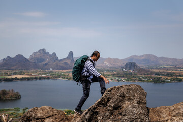 wide shot of a male traveler standing on a rocky peak, wearing a backpack and gazing at the...