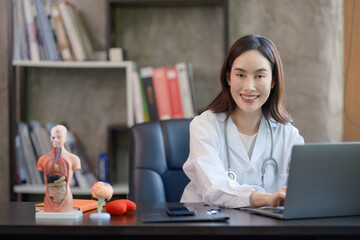 A professional female doctor in a white coat with a stethoscope, sitting and working with a laptop...