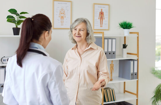 Happy, smiling senior patient talking to her nurse or doctor. Geriatrics specialist communicating with a friendly, old, grey haired woman at the medical office. Health care concept
