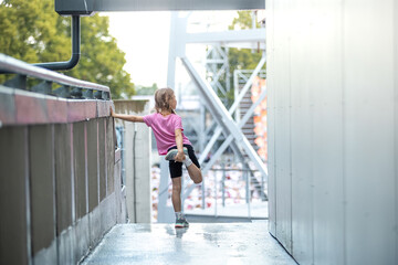 Child Stretching on Wet Walkway Near Modern Structure and Trees