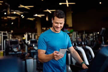 Happy sportsman using cell phone during gym workout.