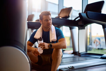 Pensive athlete having water break while exercising in health club.