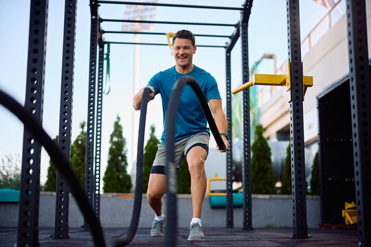 Male athlete exercising with battle ropes during cross training in outdoor gym.