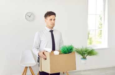 Portrait of upset male dismissed business man in formal clothes with a box of his belongings...