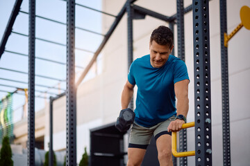 Athletic man working out with hand weight in outdoor gym.