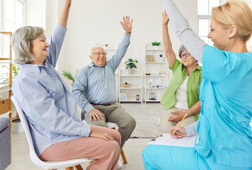 Group of elderly men and women sitting in a circle with hands up in nursing home with friendly...