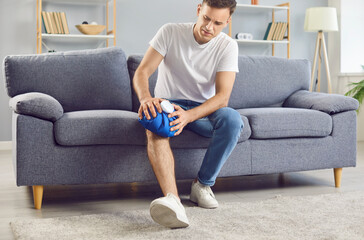 Unfortunate man injured his leg at home, feels pain and holding ice pack to his injured knee. Man...
