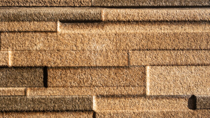 Close-up of textured golden brown stone wall tiles with a rough surface and layered horizontal pattern, ideal for backgrounds, interior design, or architectural materials.