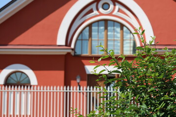 A small red building surrounded by a white fence and featuring a lone tree, suitable for use in...
