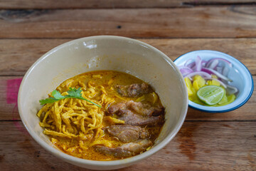 Khao Soi with fried pork served with pickled vegetables, onion, and lime. Traditional Northern Thai noodle curry dish.