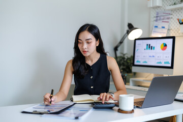 Asian businesswoman calculating financial data and taking notes in modern office