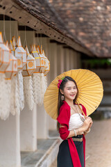Asian woman in traditional Lanna dress at Wat Intharawat, Chiang Mai. Smiling tourist with umbrella...