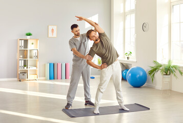 Therapist assists a patient with stretching exercises during a physiotherapy session, focusing on...