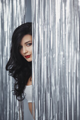 Glamorous Woman Peeking Through Silver Curtain With Bold Expression 
