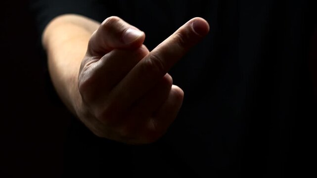 A man's hand on a black background shows an indecent aggressive gesture FUCK YOU.
A man shows his hand with a raised middle finger demonstrating his anger and aggression