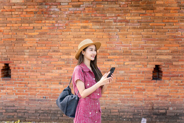 Asian woman using phone while exploring Tha Phae Gate in Chiang Mai. Young female tourist enjoying digital lifestyle during travel in Thailand.