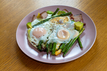 Eggs fried in a pan with asparagus, bacon, and avocado, natural, unprocessed food suitable for a ketogenic diet.