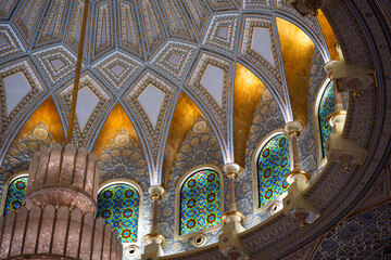 An ornate ceiling with stained glass windows, intricate patterns, and a large chandelier. No people are present