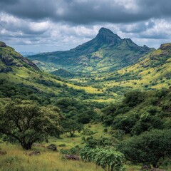 Fototapeta premium Lush green valley nestled between rolling hills under a dramatic, cloudy sky; a prominent peak dominates the background