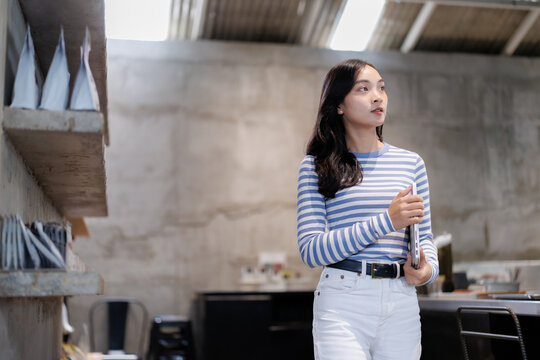 Young asian woman holding laptop and thinking in coffee shop