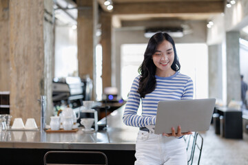 Smiling asian businesswoman using laptop in modern cafe