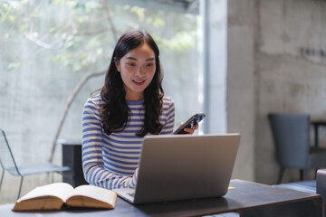 Young asian woman working remotely using laptop and smartphone in modern office space